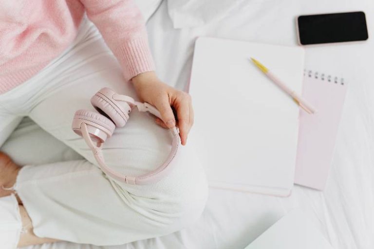 Lifestyle Blog Niches: How To Niche It Down And Be Successful 25 Lifestyle blog niches - woman's hands with a notebook and headphones on a white bed.